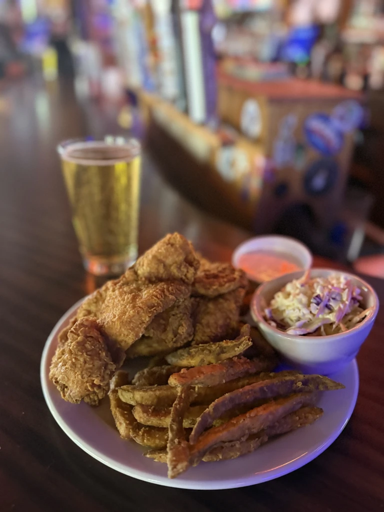 Plate of fried chicken, fries, coleslaw, and beer at a dim bar.
