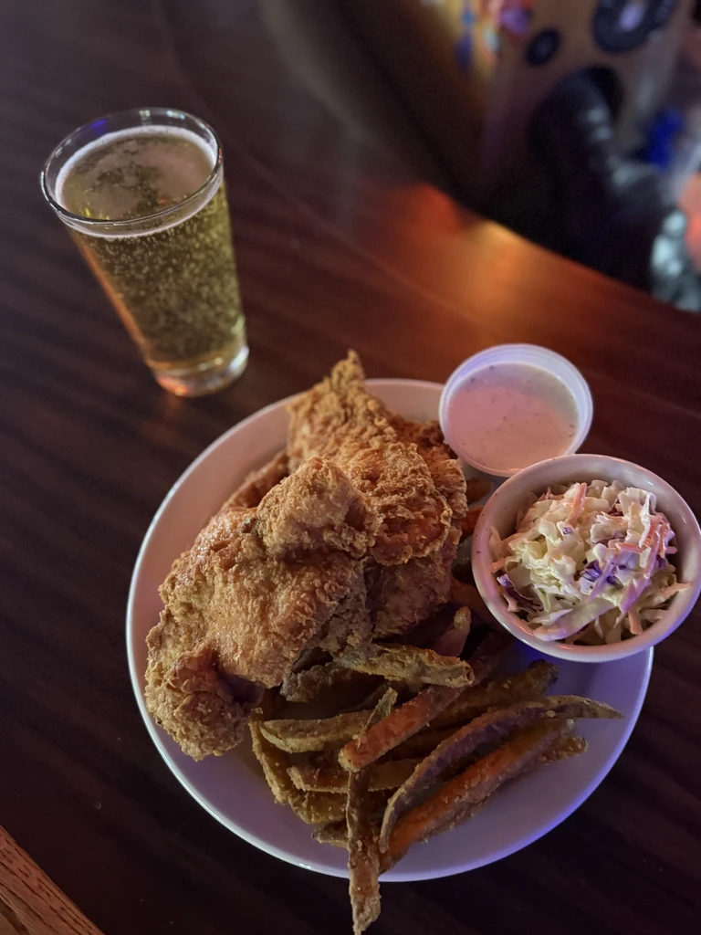 Fried chicken, fries, coleslaw, sauce, and beer on a wooden surface.