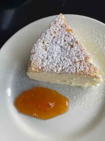 Triangular slice of cake with powdered sugar and orange jam on a plate.