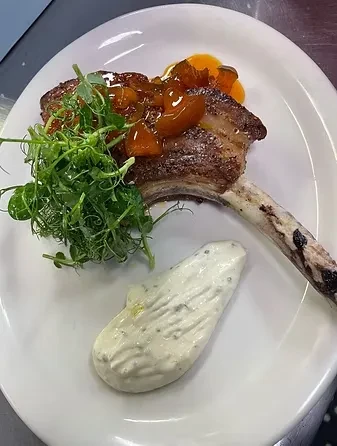 Seared meat chop with reddish relish, green sprouts, and white sauce.