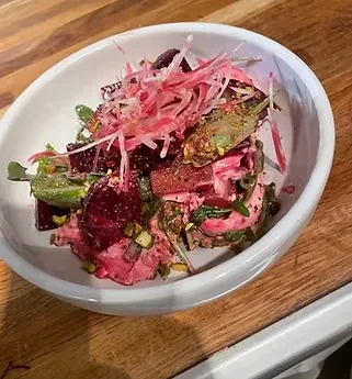 Overhead beet salad with pink dressing, pickled onions, and pistachios.