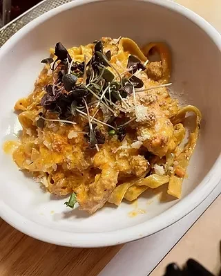 Close-up of broad flat pasta with creamy orange sauce, cheese, microgreens.