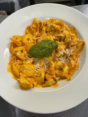 Close-up, top-down: Tortellini with orange sauce, green pesto, and grated cheese.