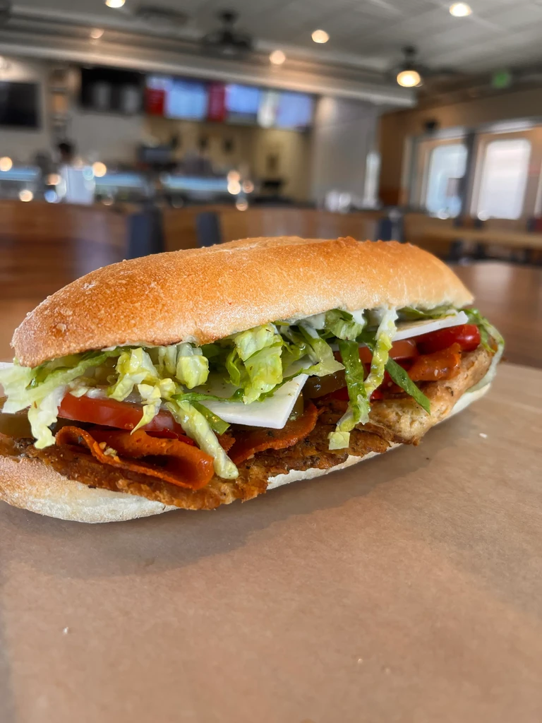 Large, golden sub sandwich with meat, cheese, and vegetables at a deli.