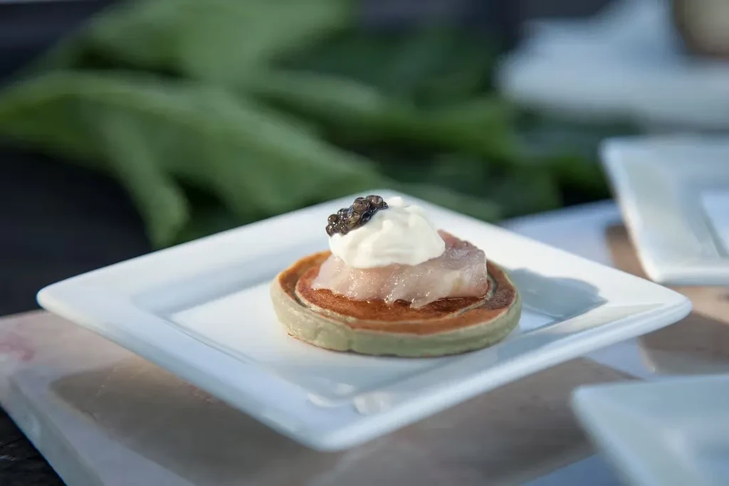 Appetizer blini with salmon, cream, and caviar on a white plate.