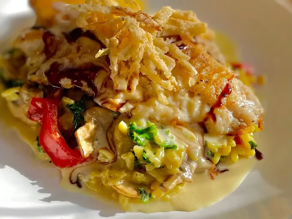 Close-up of plated fillet with melted cheese, crispy onions, and creamy vegetables.
