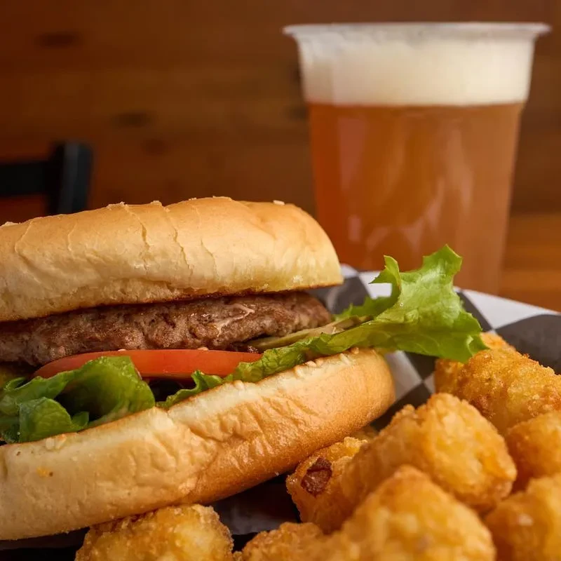 Hamburger, tater tots, and beer served in a checkered basket.