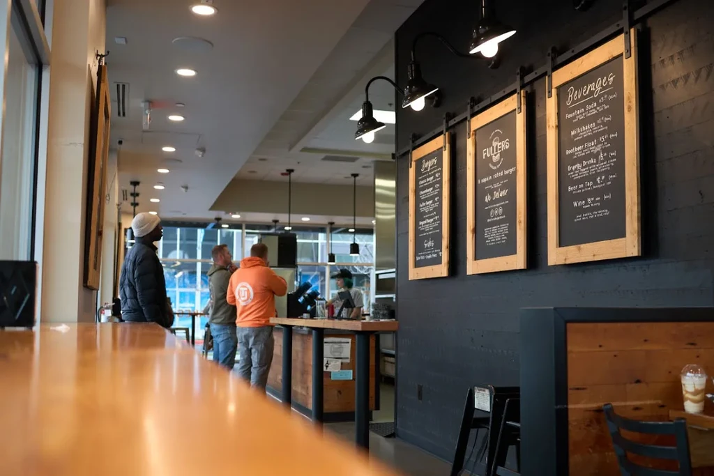 Modern restaurant interior with people queuing at counter and rustic menu boards.