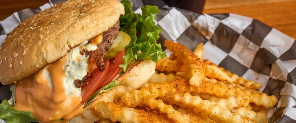 Large burger with dripping sauces and seasoned crinkle-cut fries.