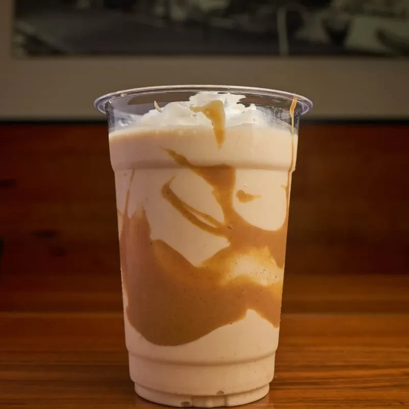 Caramel swirl frappe with whipped cream in a clear plastic cup.