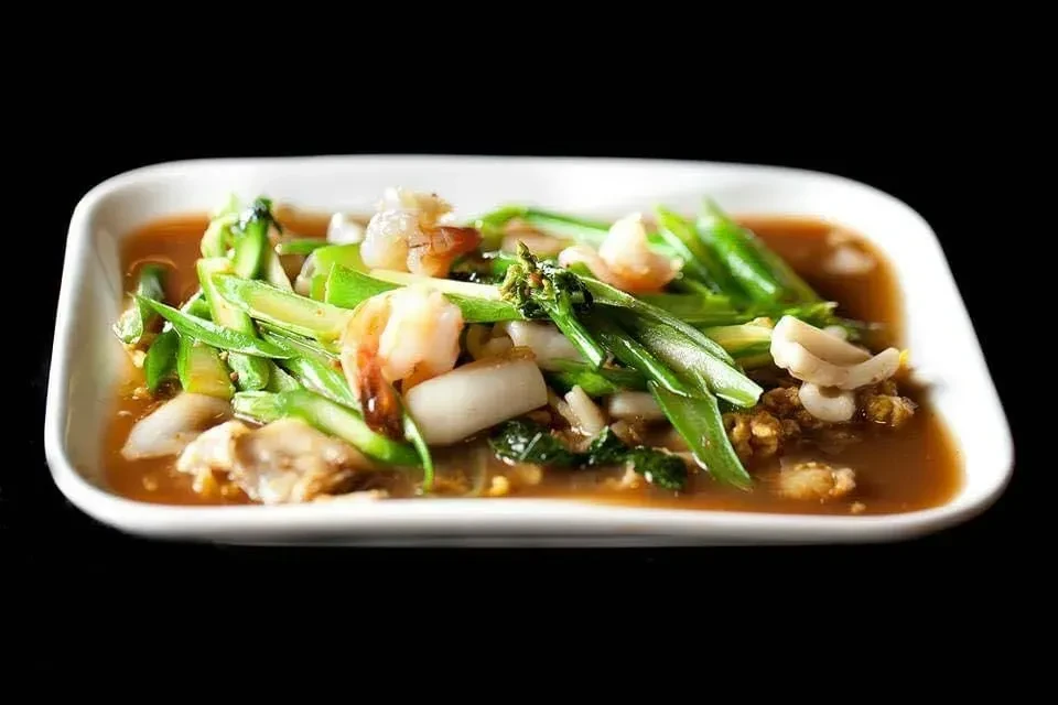 Shrimp, squid, and green vegetables in reddish-brown sauce on white plate.