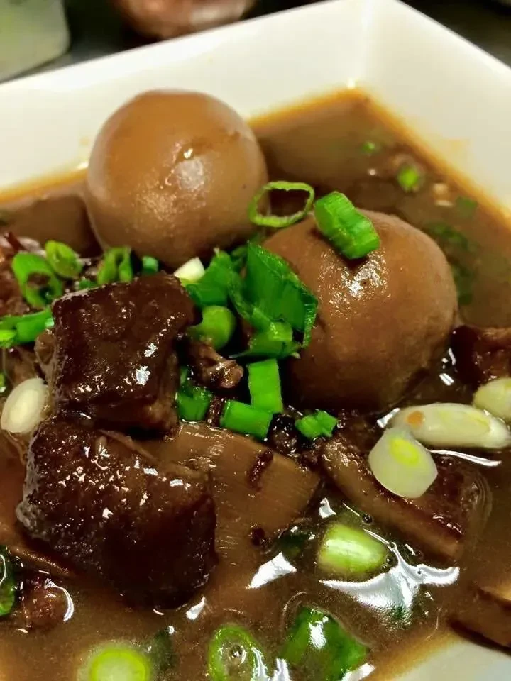 Braised eggs and stewed meat in dark sauce, garnished with green scallions.