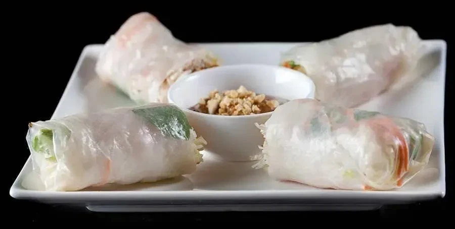 Four fresh Gỏi cuốn spring rolls with peanut sauce on a white plate.