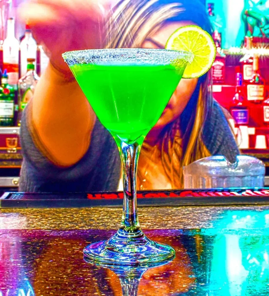 Vibrant green martini with lime and salted rim on a reflective bar.