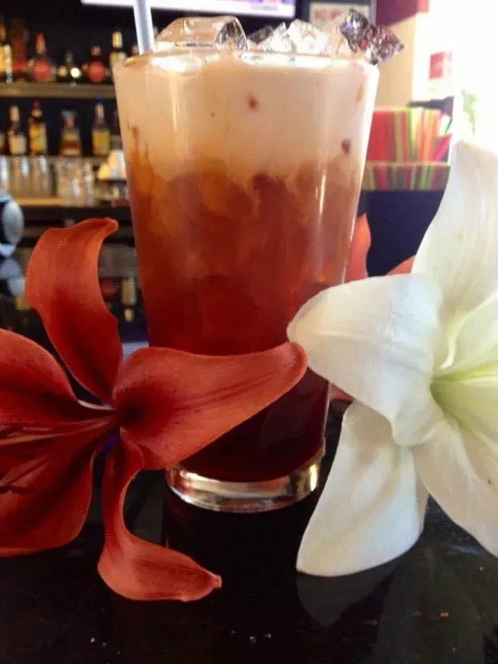 Layered iced tea with straw, framed by red and white flowers.