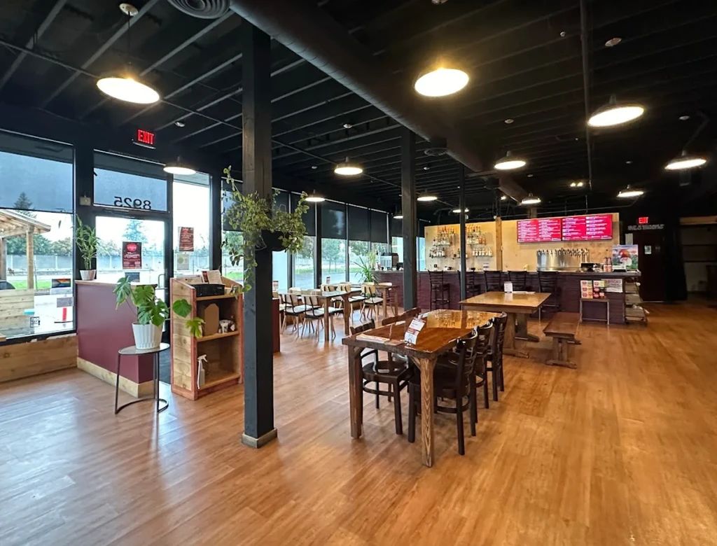 Empty modern industrial-style restaurant interior, prominent bar, wooden tables, plants.