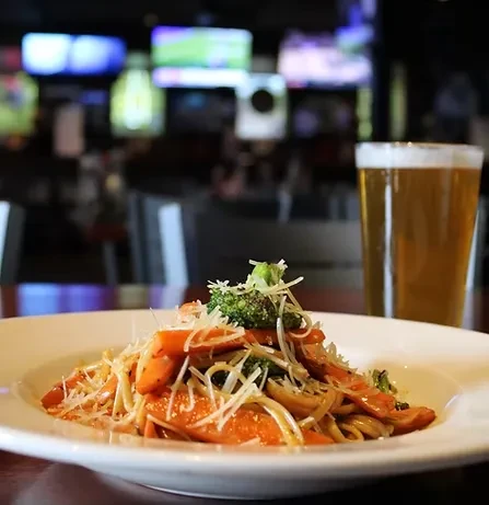 Pasta with vegetables and cheese, a beer, in a sports bar.