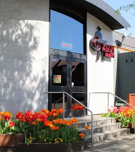 G-MAN BREWERY entrance with neon signs and colorful tulip planters.
