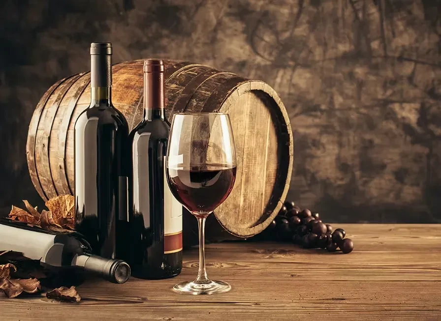 Still life of wine bottles, red wine glass, grapes, leaves, barrel.