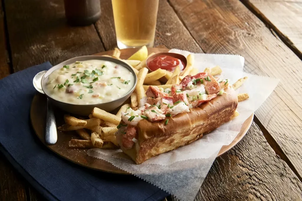 Lobster roll, french fries, and clam chowder on a rustic table.