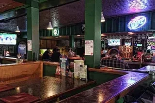 Dimly lit bar interior with patrons, TVs, beer taps, and neon signs.