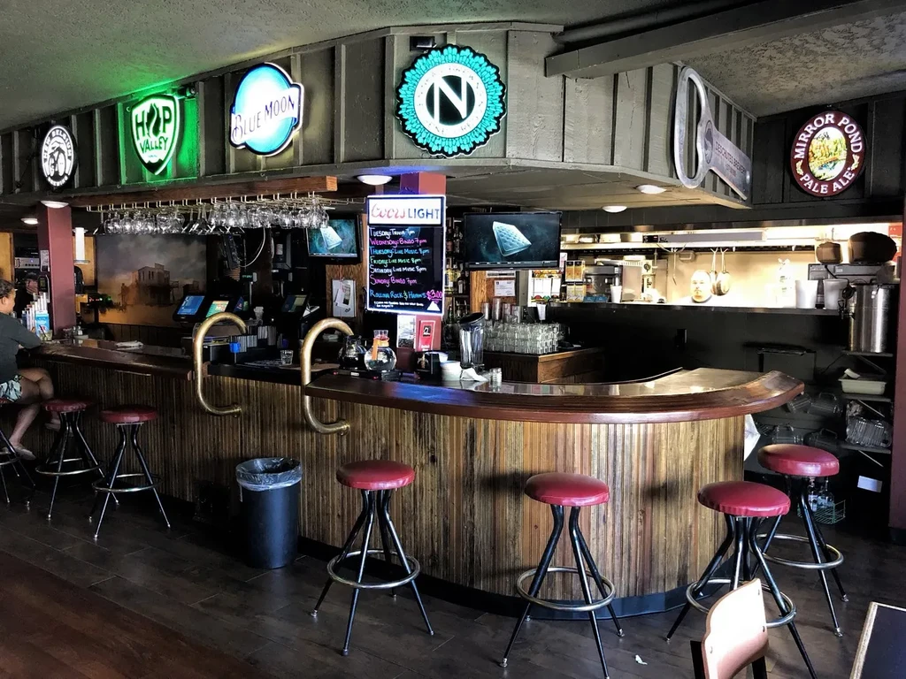 Casual bar interior with curved wood counter, red stools, and neon signs.