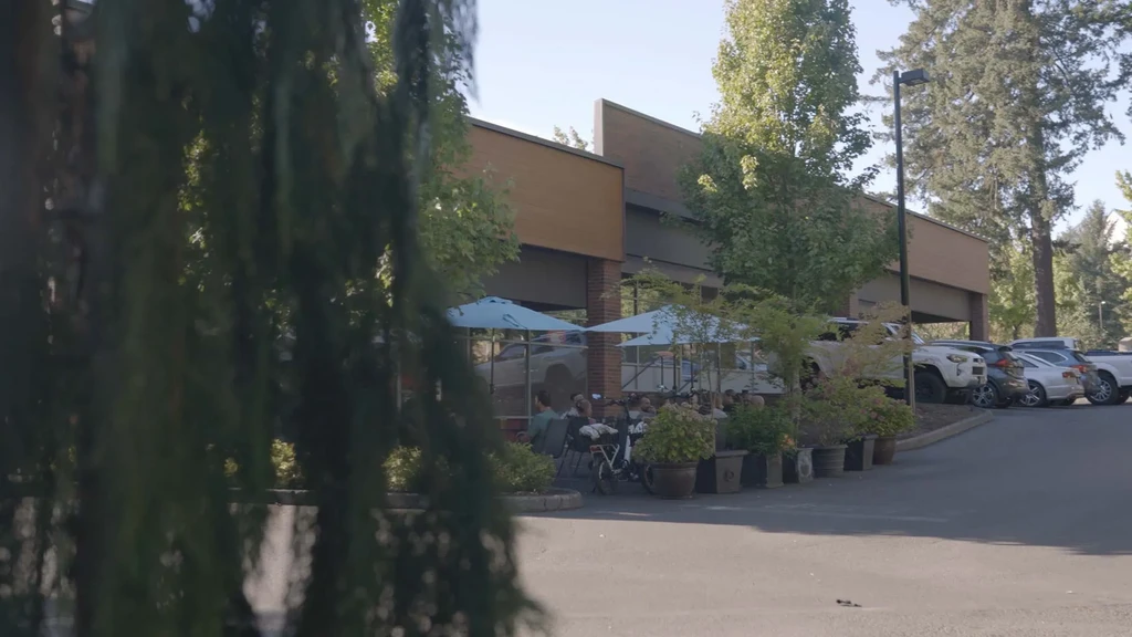 Restaurant patio with people, blue umbrellas, and a modern brick building.