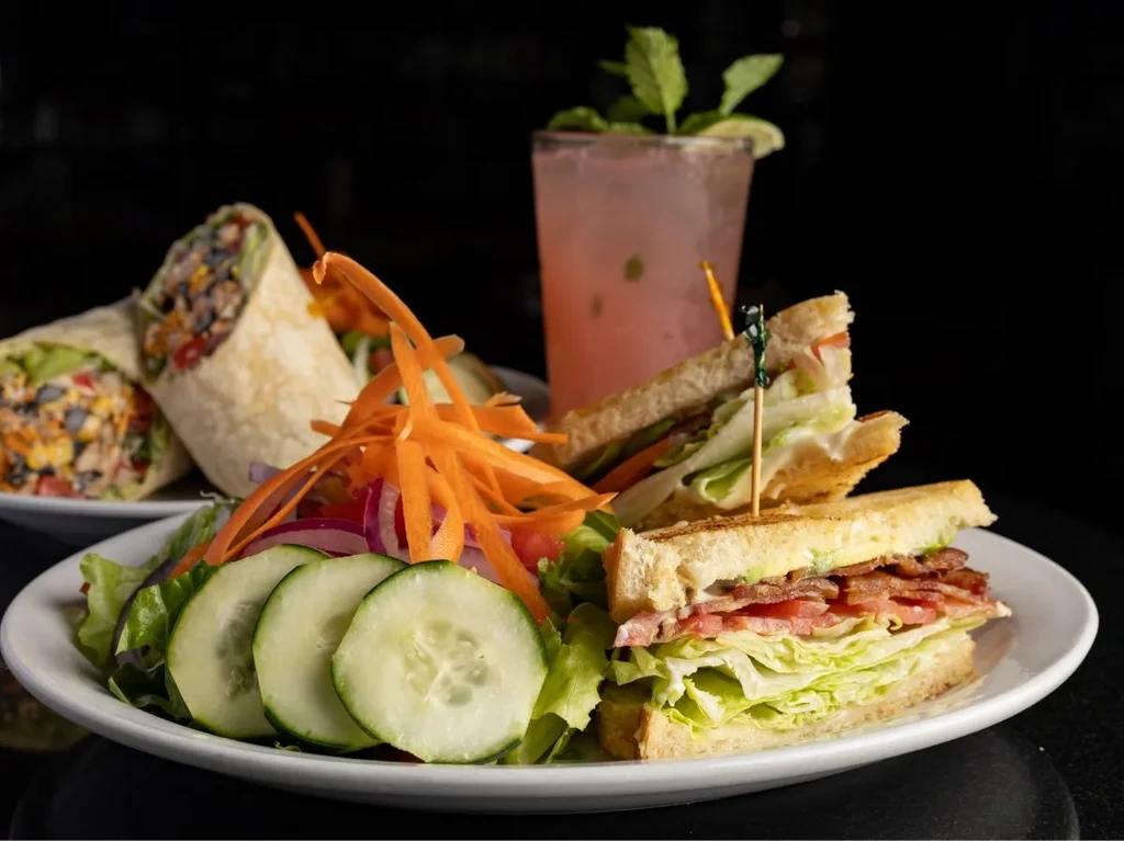 Club sandwich, fresh salad, pink drink, and wrap on a table.