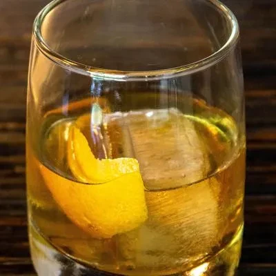 Amber cocktail in short glass, square ice, citrus peel.