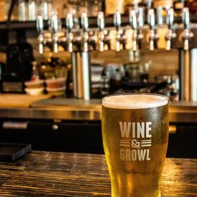 Frosty beer glass with foamy head and "WINE & GROWL" logo.