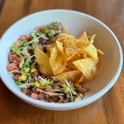 Tuna poke with microgreens and crispy chips in a white bowl.
