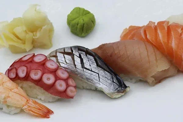 Nigiri sushi, pickled ginger, and wasabi on a white plate.