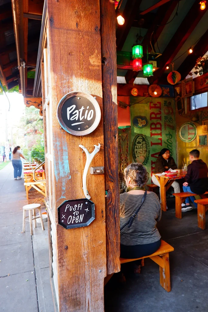 Rustic restaurant entrance with weathered 'Patio' sign and colorful interior.