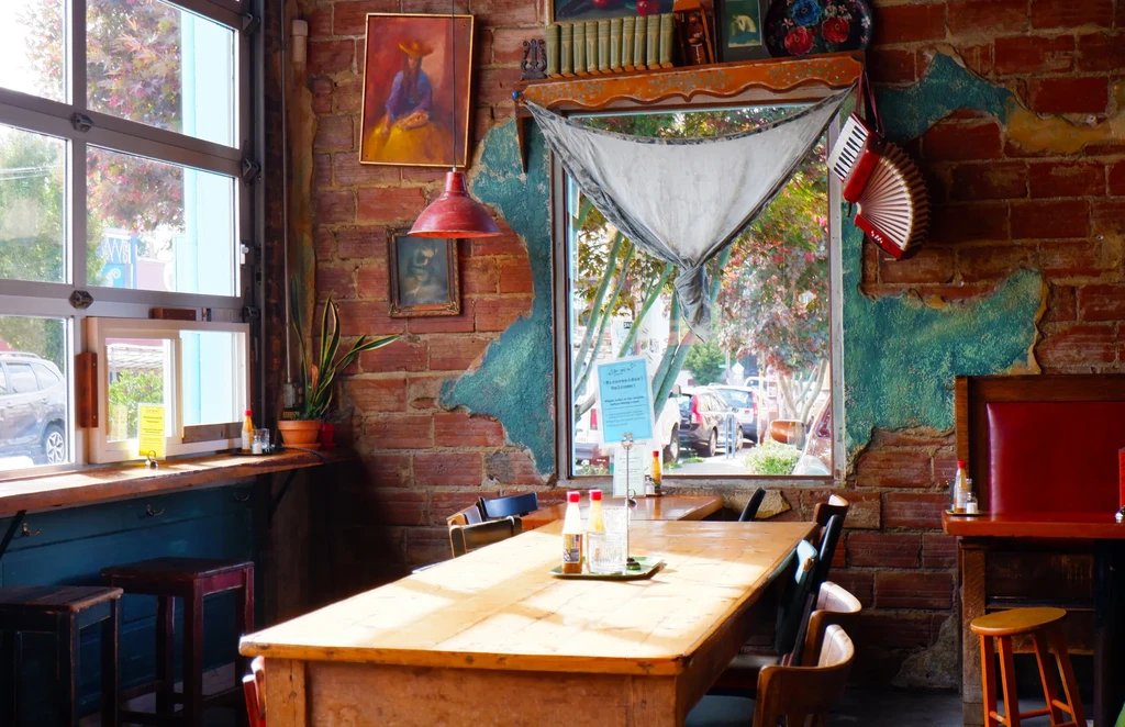 Restaurant interior with peeling teal plaster, brick wall, and communal table.