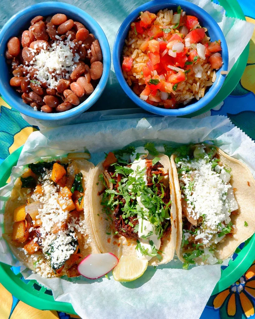 Three tacos, pinto beans, and rice in a green basket.