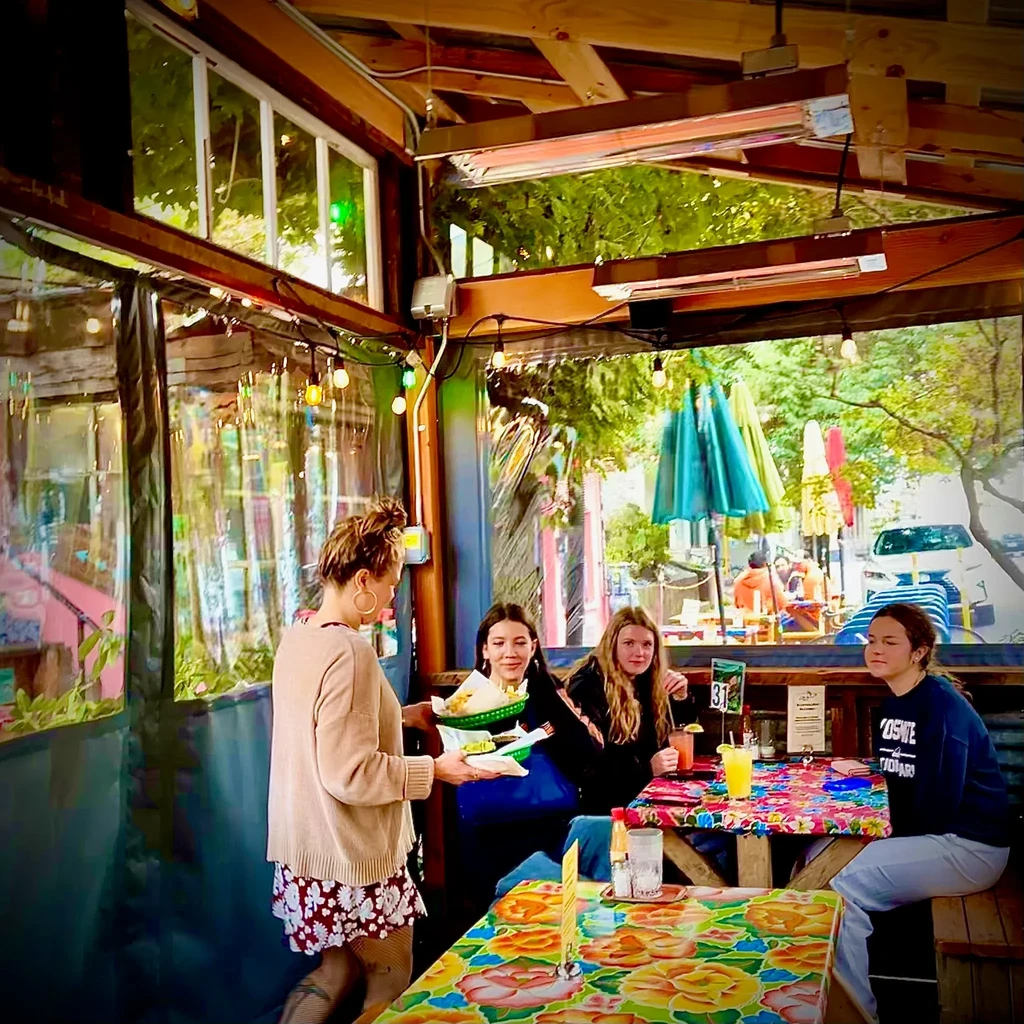 Server delivers food to three women in a colorful outdoor restaurant patio.