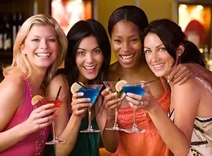 Four women cheerfully pose with cocktails in a bar.