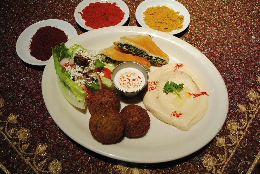 Mediterranean platter with falafel, hummus, spanakopita, salad, and dipping sauce.