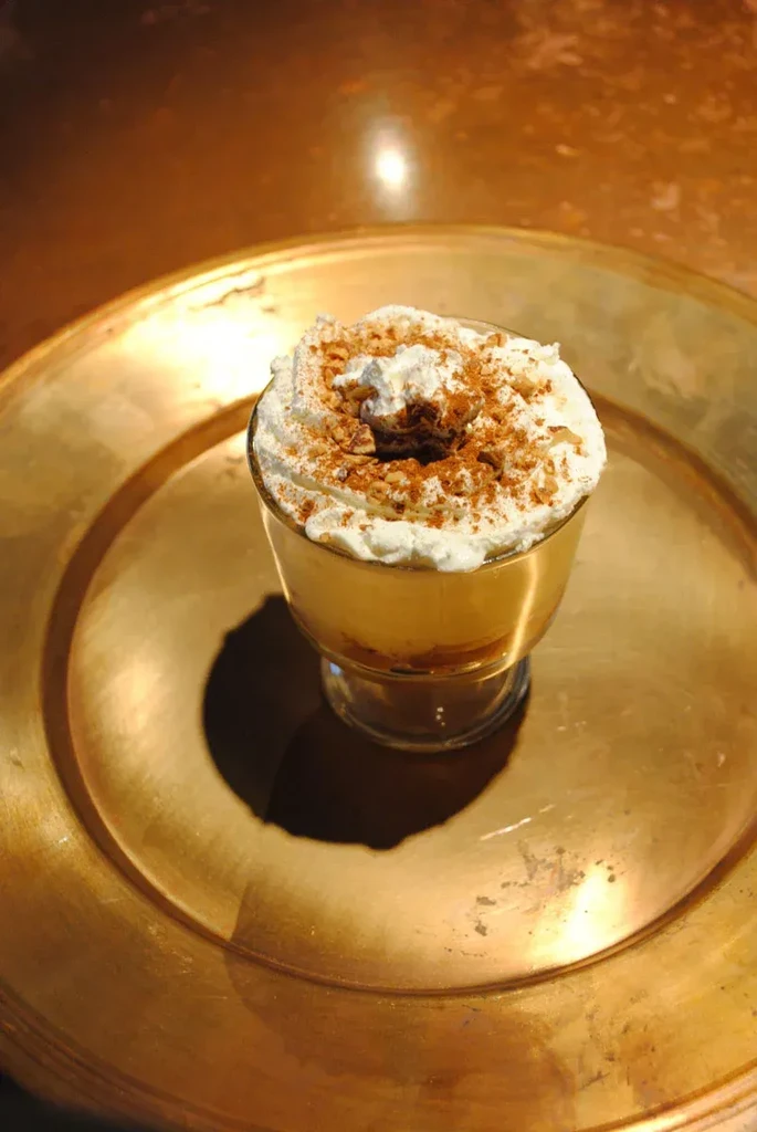 Whipped cream-topped dessert in a stemmed glass with nuts and powder.