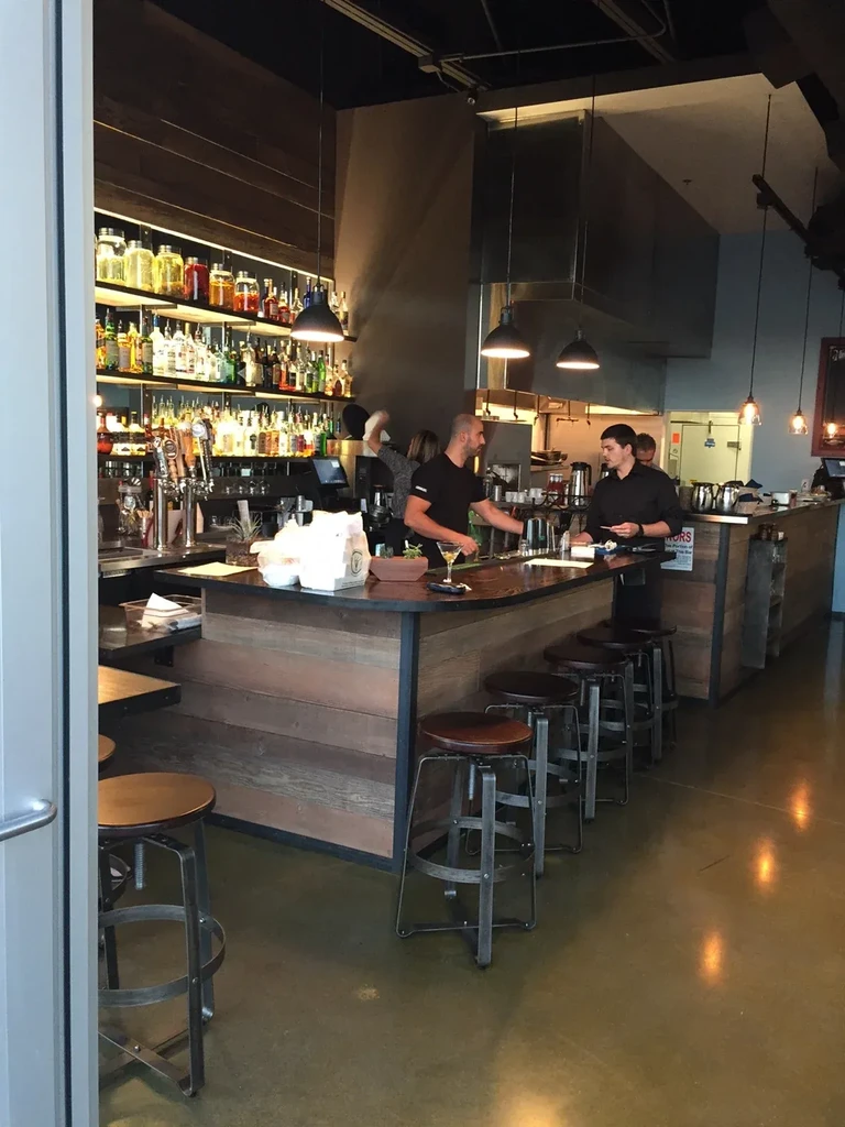 Two bartenders work behind a modern bar with illuminated liquor shelves.