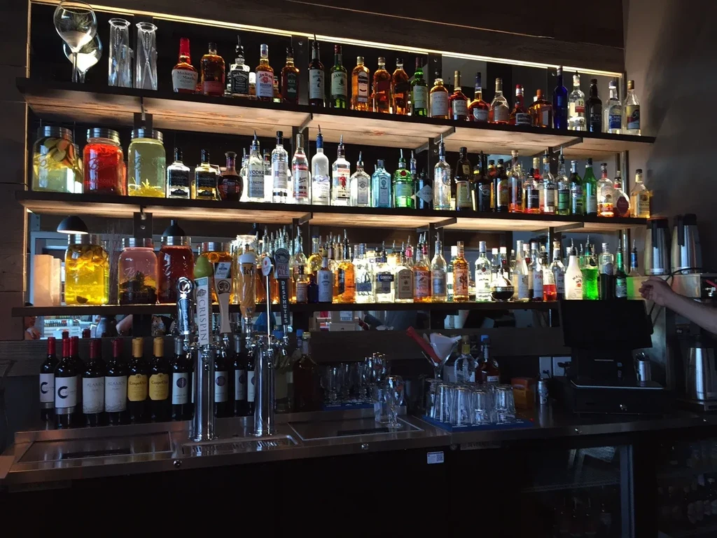Well-stocked bar with illuminated shelves of spirits, infused jars, and beer taps.