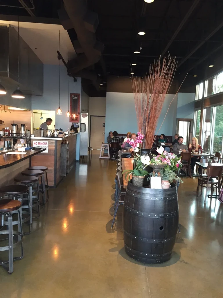Modern restaurant with bar, plant-decorated barrel, diners, 'NO MINORS' sign.