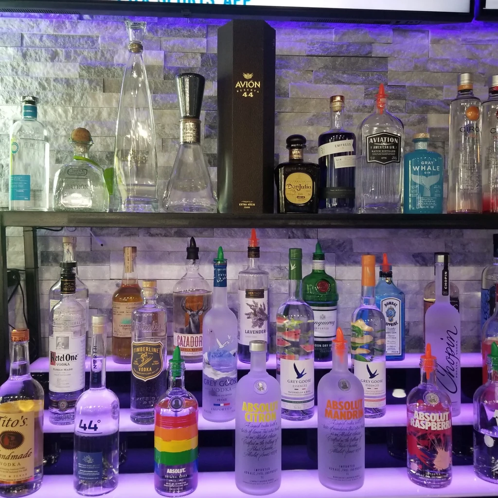 Well-stocked bar shelves with various liquor bottles and purple LED lighting.