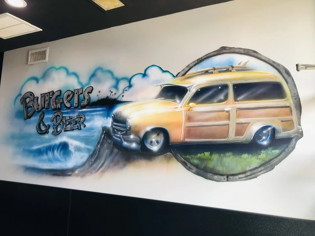 Airbrushed mural of woody wagon, surfboard, ocean, and "BURGERS & BEER".