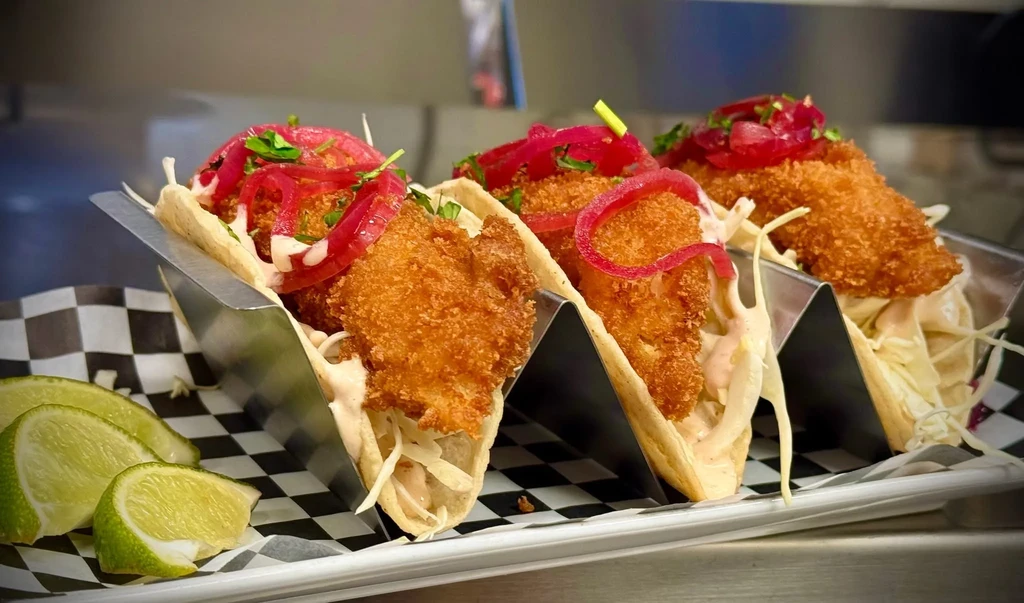 Three crispy fried fish tacos with toppings and lime.