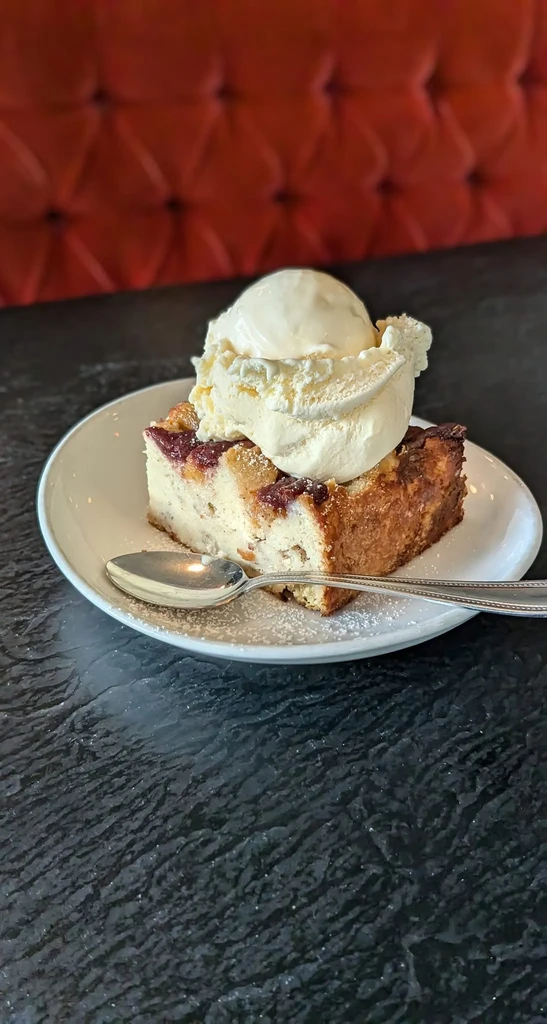 Slice of berry bread pudding with melting vanilla ice cream and spoon.
