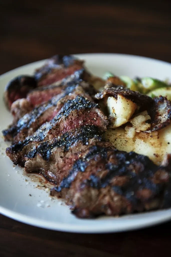 Seasoned medium-rare steak with grill marks, potatoes, and vegetables.