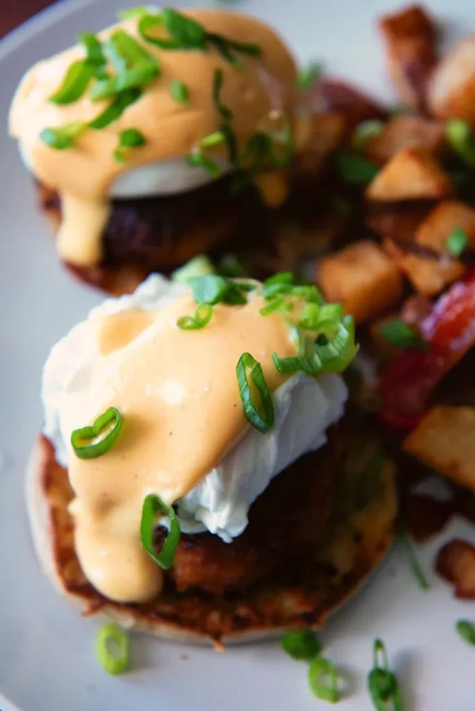 Two poached eggs with hollandaise, savory patties, and potatoes.
