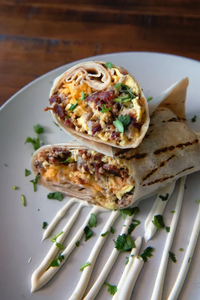 Grilled breakfast burrito, cut showing eggs, cheese, bacon, and herbs.