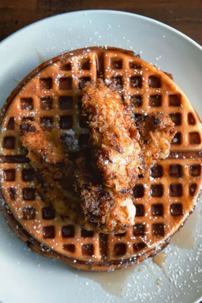 Plate of crispy fried chicken and waffles with syrup and sugar.
